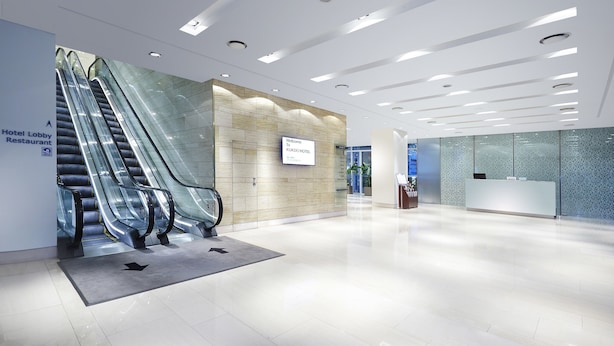A modern hotel lobby with escalators, a reception desk, and a sign for the hotel lobby and restaurant. - Hotel Kukdo (Seoul)