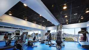 A modern gym with various exercise equipment, large windows, and a view of mountains. - Hotel Kukdo (Seoul)