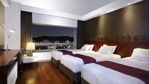 A hotel room with two beds, a desk, a lamp, and a view of a cityscape at night. - Hotel Kukdo (Seoul)
