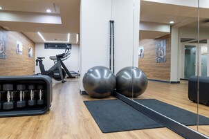 Gimnasio con equipo de ejercicio, incluyendo mancuernas, una elíptica y pelotas de ejercicio grandes.