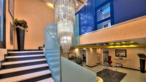 A modern interior with a staircase, a chandelier, and a glass table with chairs. - Central Park Hotel Modena (Modena)