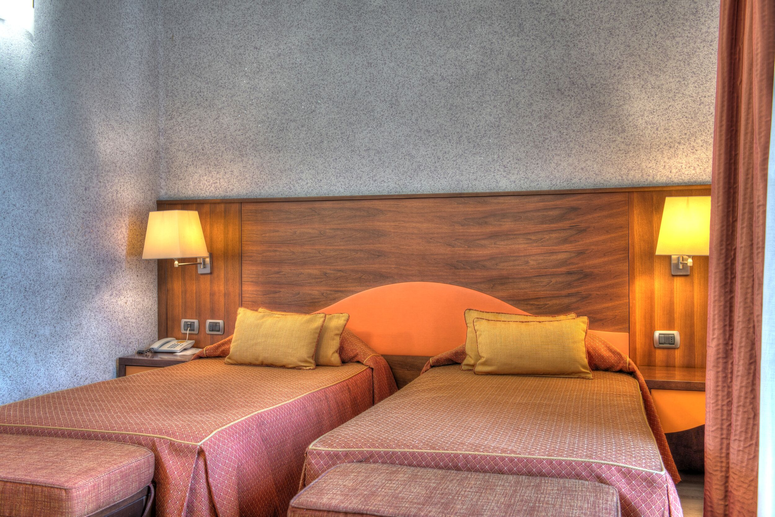 Een hotelkamer met twee bedden, een houten hoofdbord en bedlampjes.