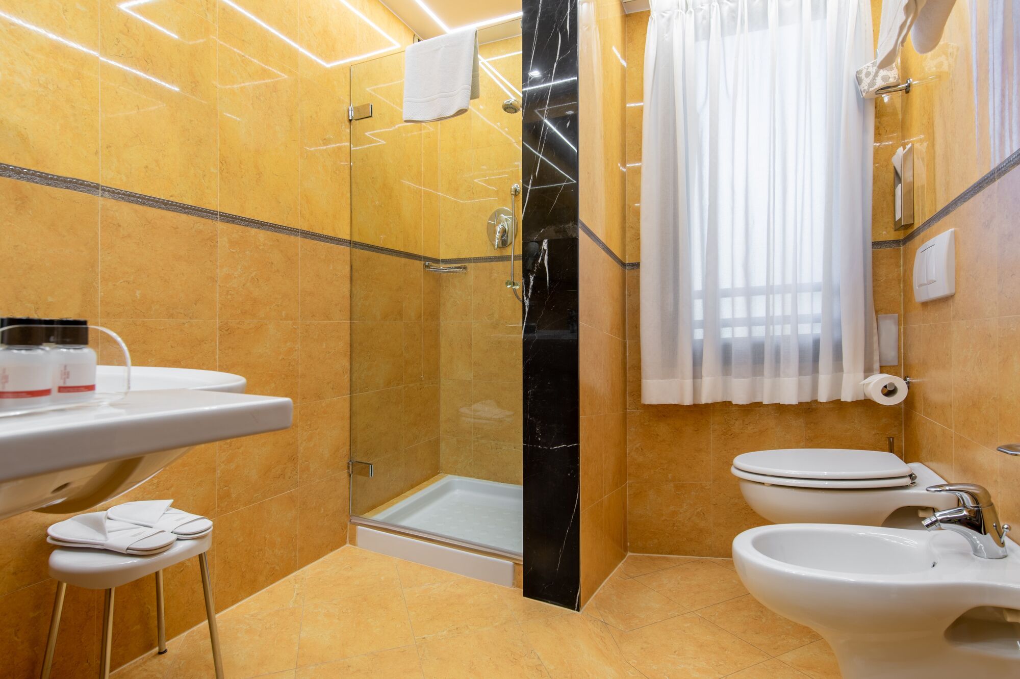 Un bagno moderno con doccia vetro-muraria, un water, un bidet e un lavandino.