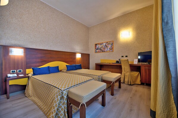 A hotel room with two beds, a desk, a chair, a TV, and a painting on the wall.
