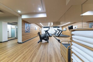 Ein Fitnessraum mit Trainingsgeräten, Holzboden und einem an der Wand befestigten Handtuchhalter.