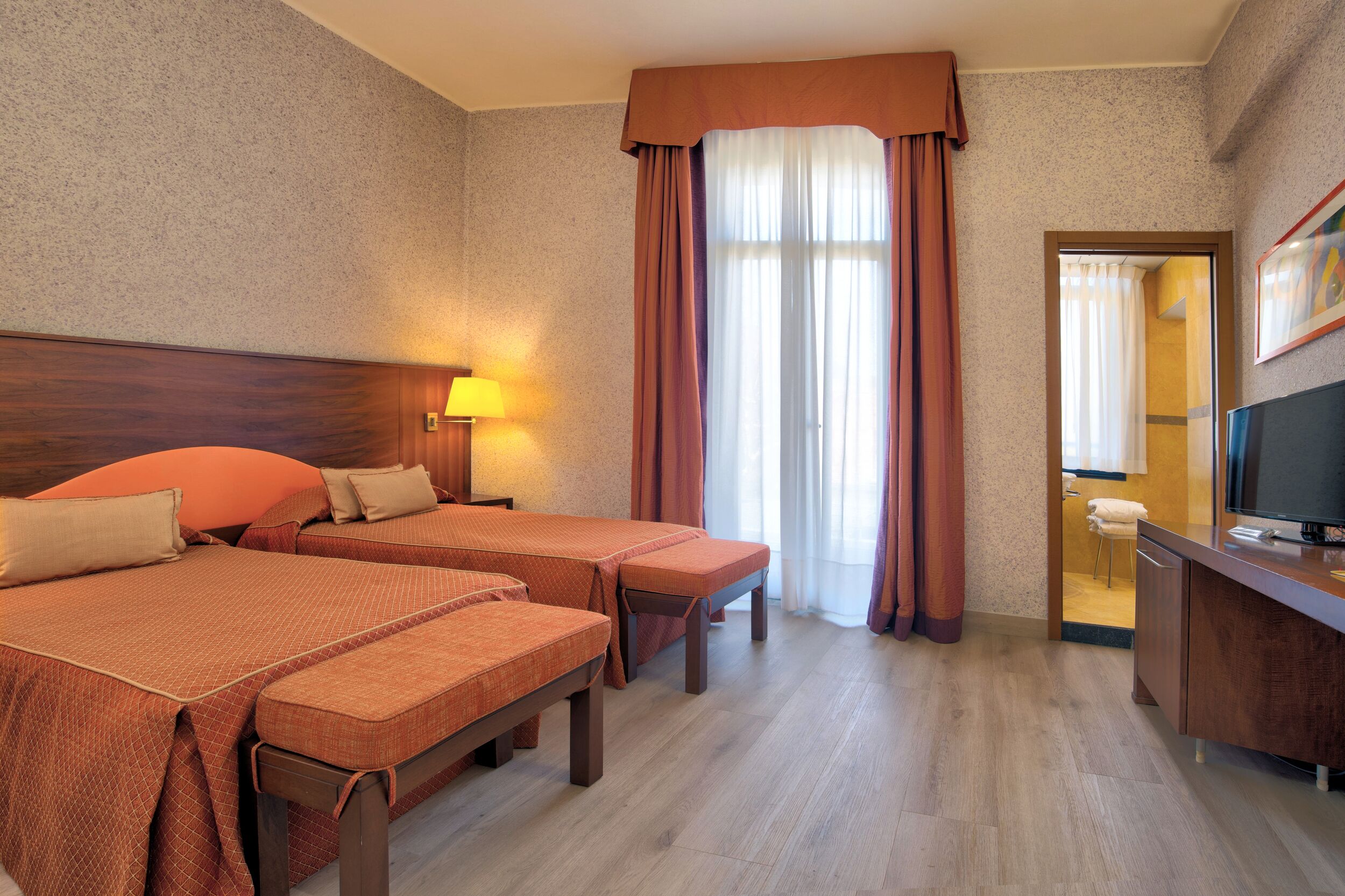 A hotel room with two beds, a desk, a television, and a bathroom visible through an open door.
