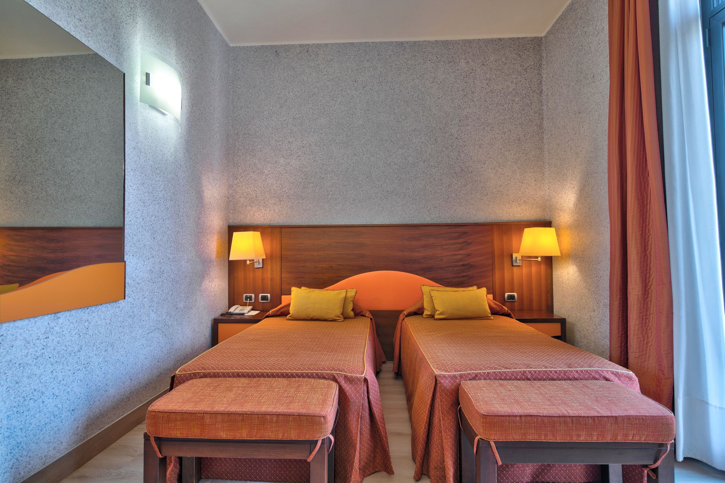 A hotel room with two beds, a wooden headboard, nightstands with lamps, and a large mirror on the wall.
