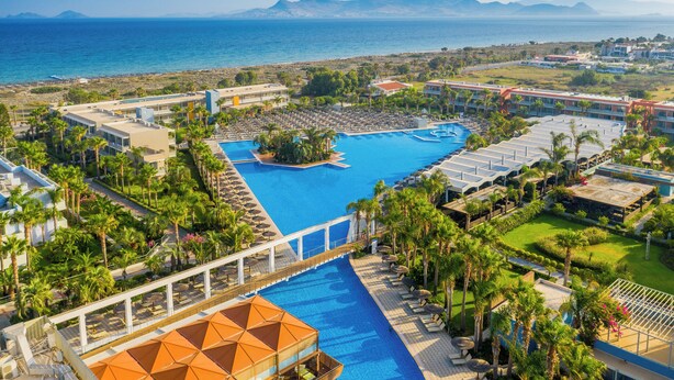 A resort with a large swimming pool, palm trees, and a view of the sea.