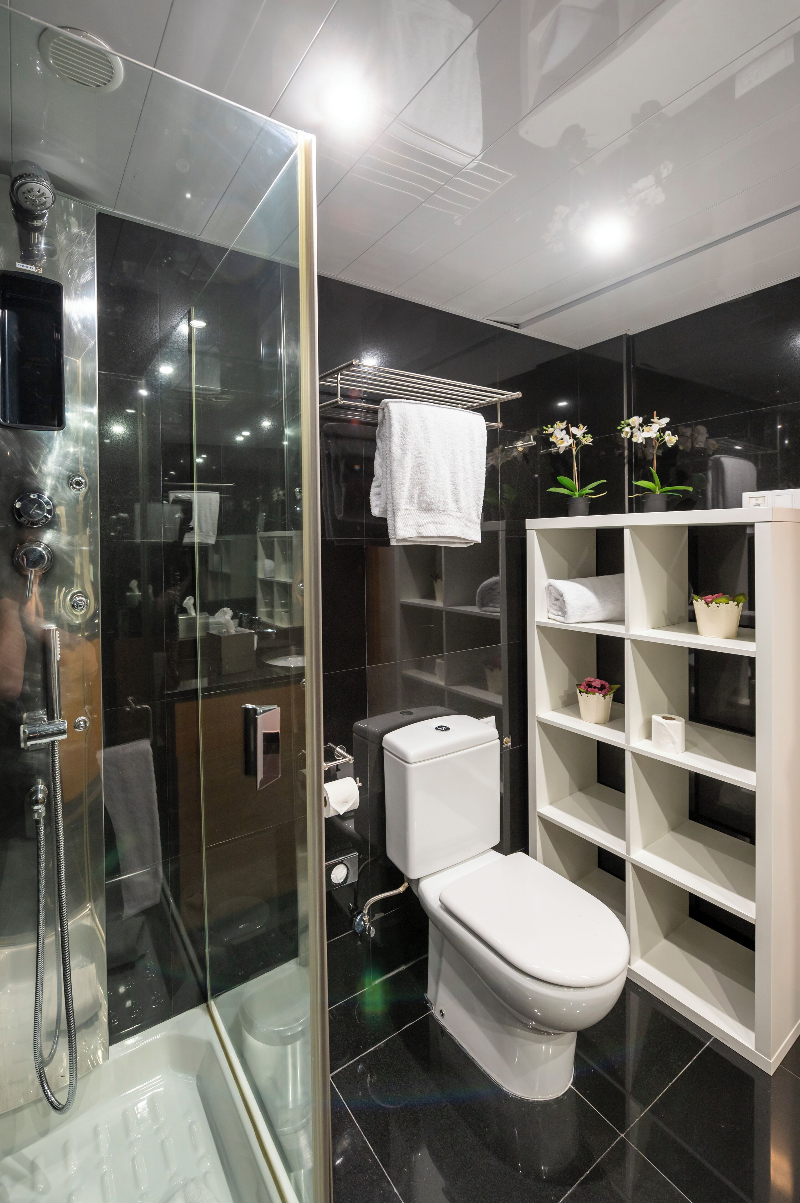 Une salle de bain moderne dotée d’une douche à parois de verre, de toilettes blanches et d’une étagère intégrée où sont rangées les serviettes et les articles de toilette.