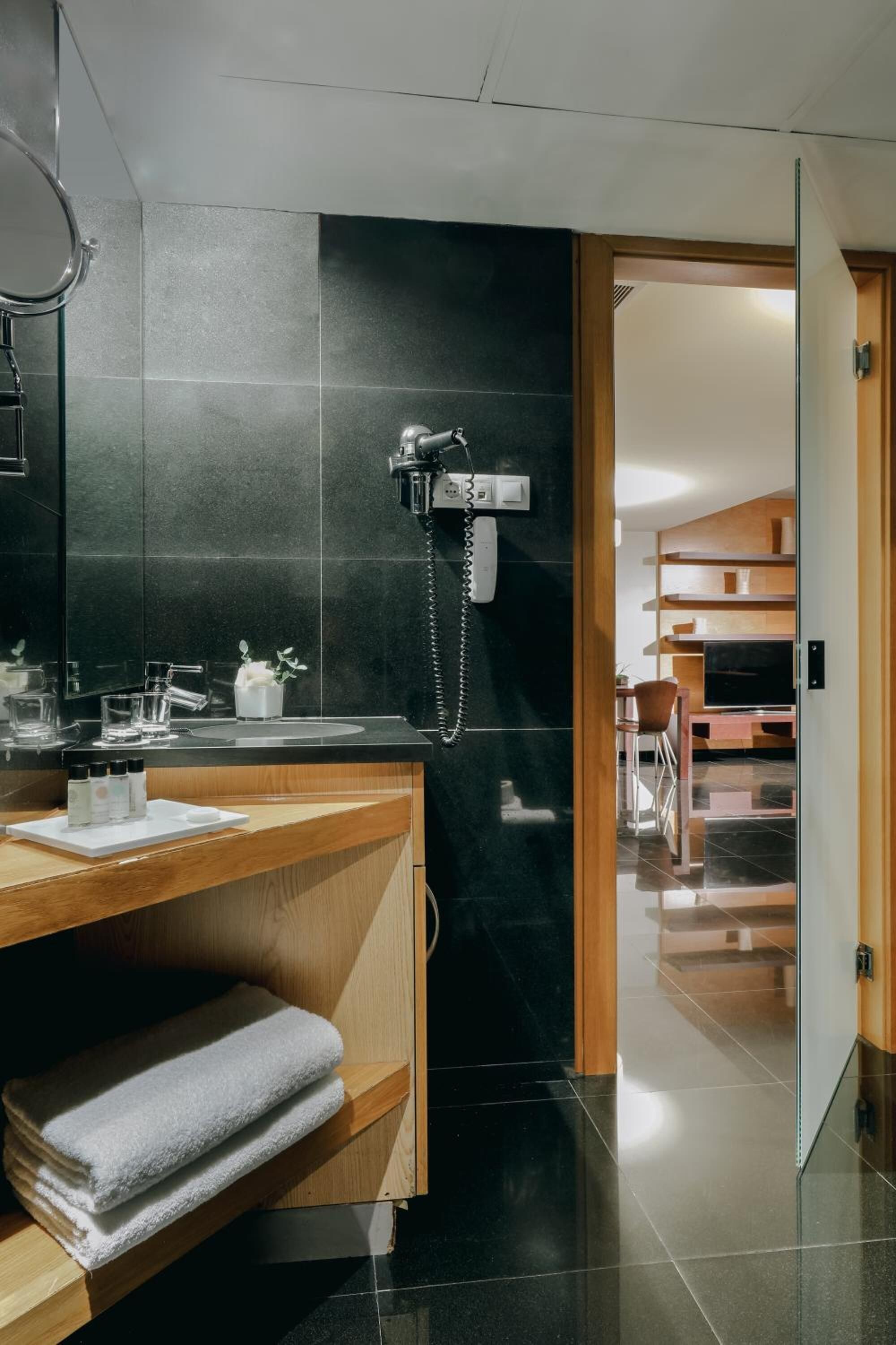 A modern bathroom with a black tiled wall, a wooden vanity, a sink, and a telephone.