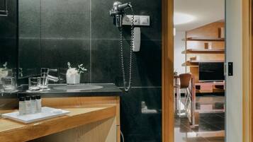 A modern bathroom with a black tiled wall, a wooden vanity, a sink, and a telephone.