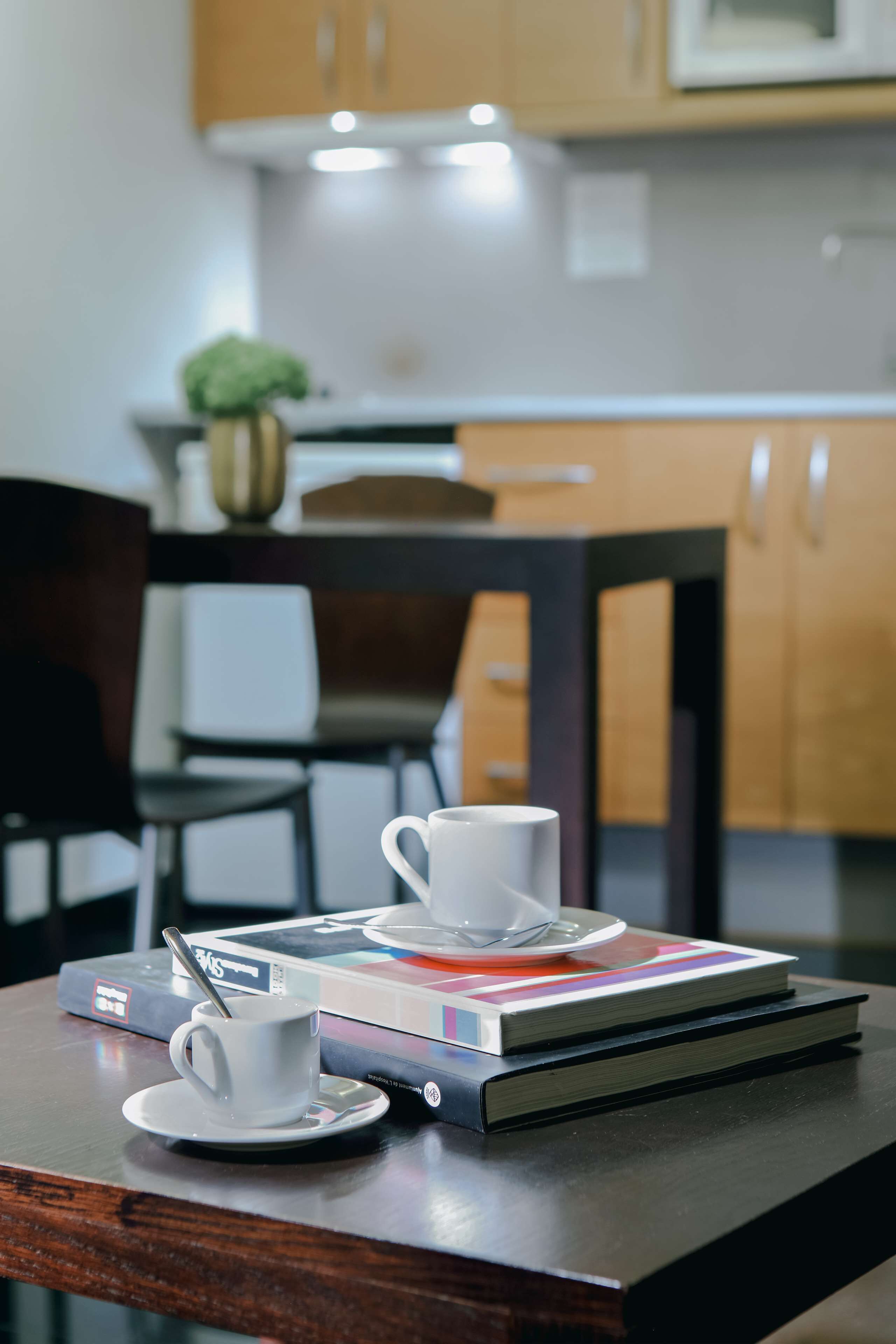 Una mesa con una taza y platillo blancos, una cuchara y un libro.