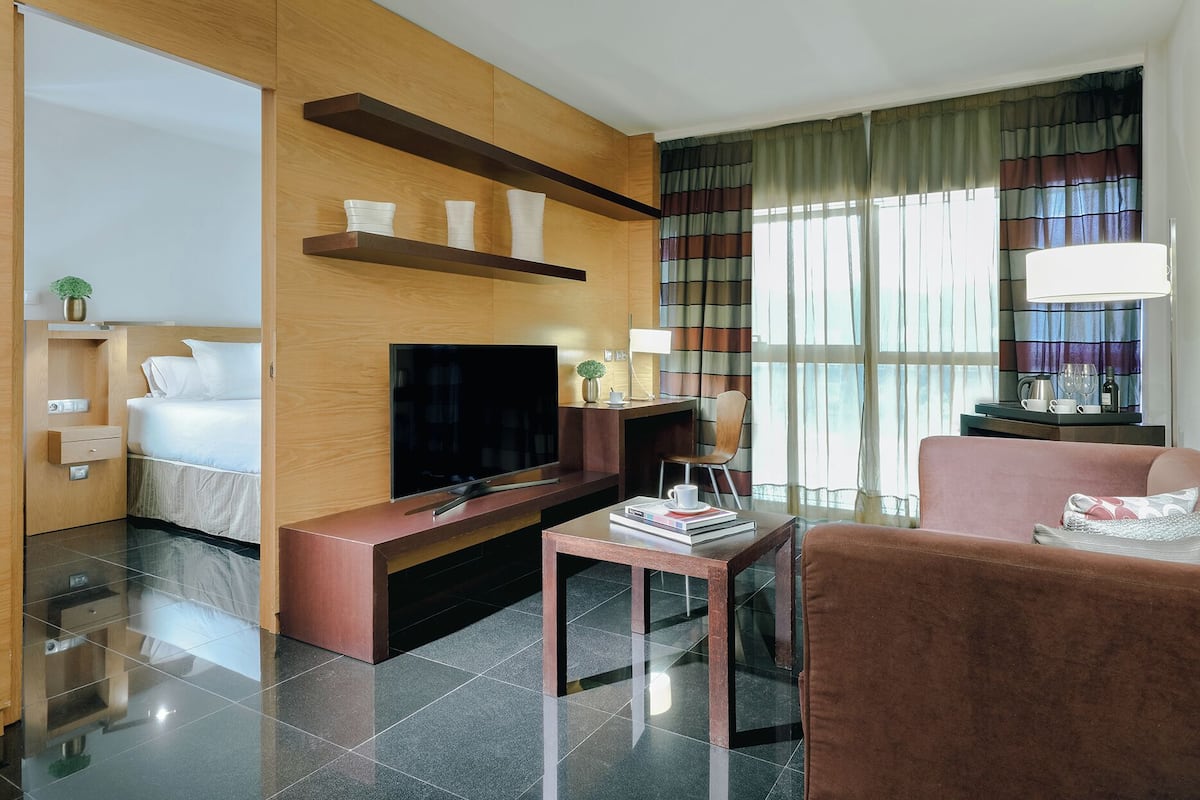 A modern hotel room with a flat-screen TV, a sofa, a coffee table, and a TV stand.