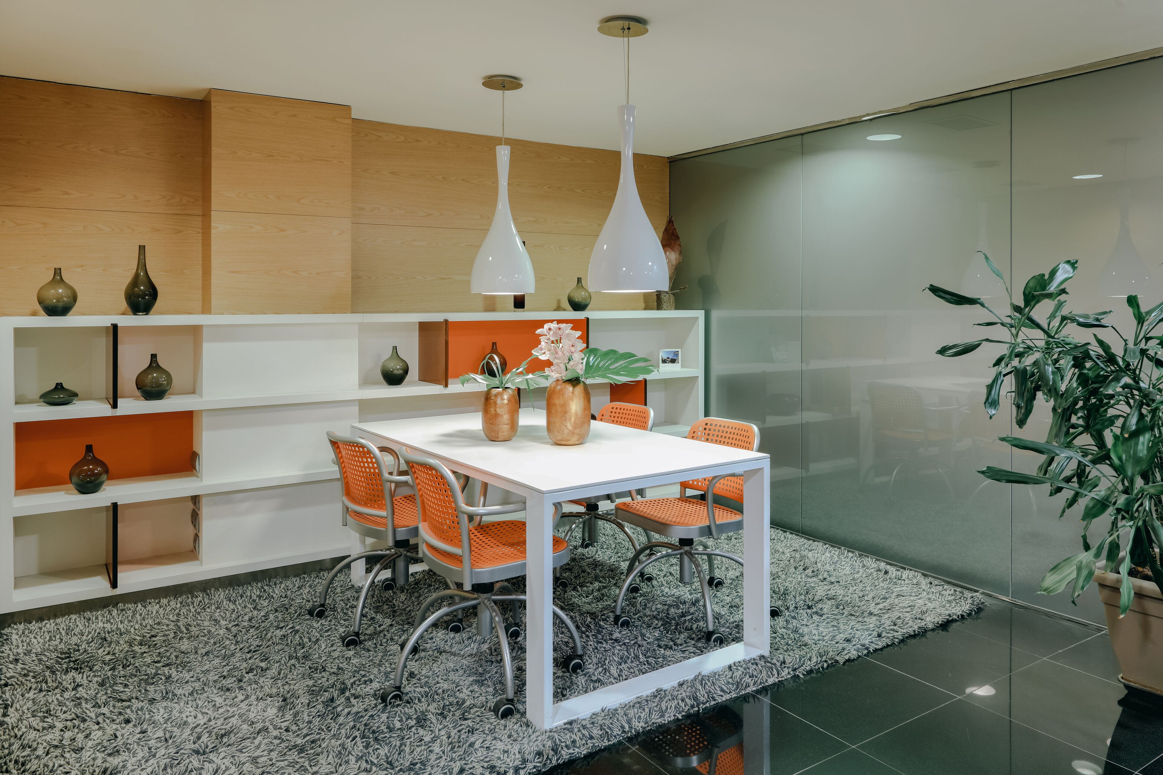 Una sala de reuniones moderna con una mesa blanca, sillas naranjas y jarrones decorativos.