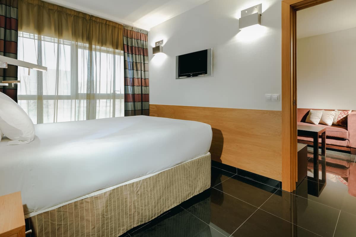 A hotel room with a large bed, a television mounted on the wall, and a small seating area with a sofa.