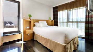 Habitación de hotel con una cama grande, una mesita de noche de madera, una pequeña mesa, una ventana con cortinas y vistas al exterior.