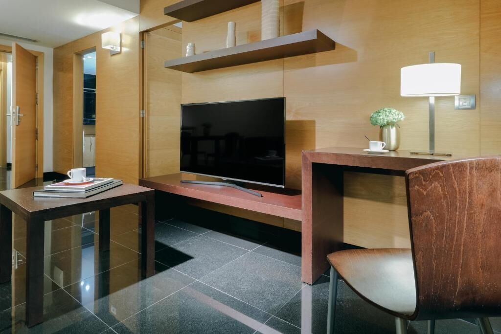 Una habitación de hotel moderna con una televisión de pantalla plana, una mesa consola de madera, una silla y una mesita con una taza y un libro.