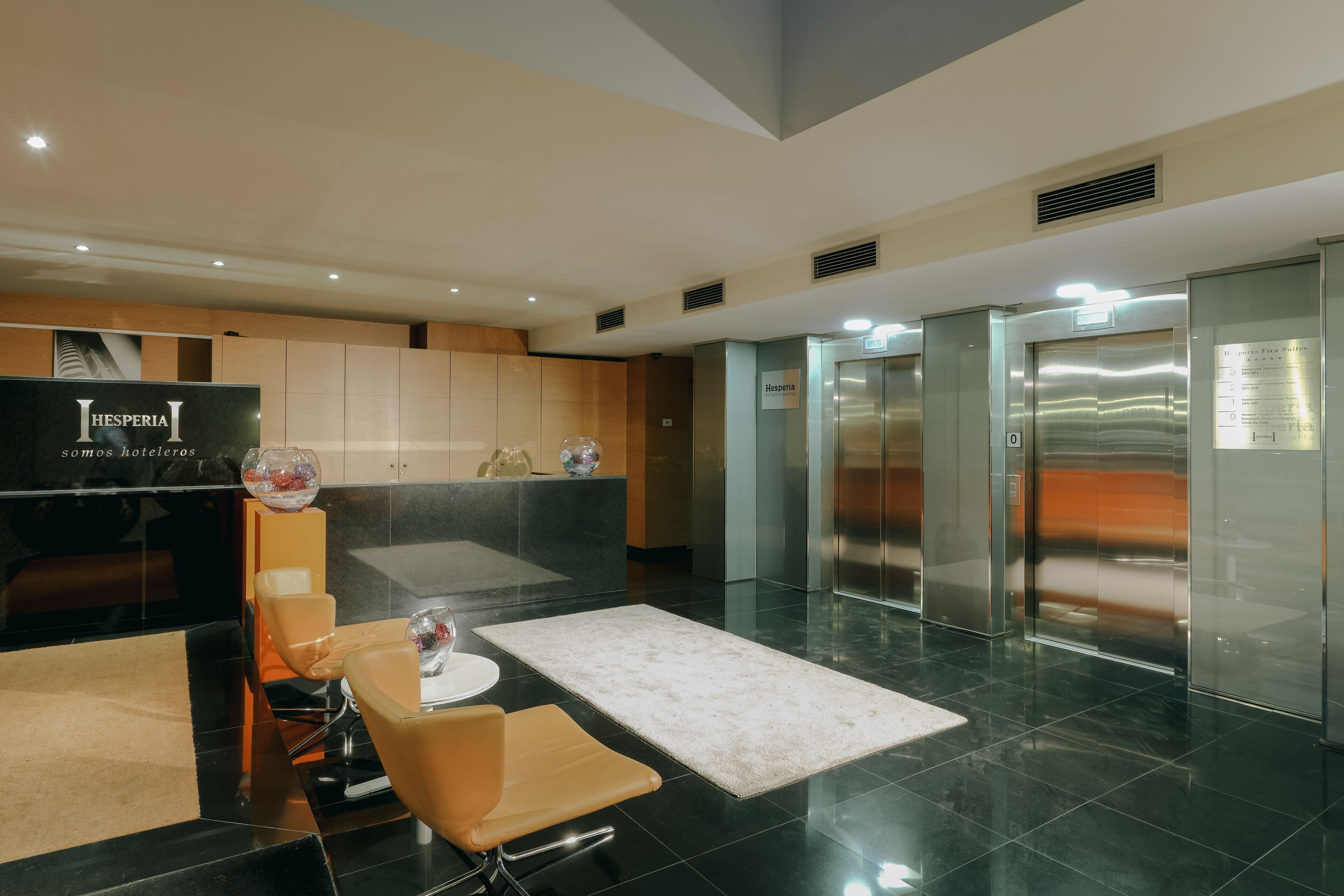 A modern hotel lobby with a reception desk, seating area, and elevators.