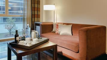 Quarto de hotel com um sofá marrom, um suporte com uma garrafa, copos e uma cafeteira.