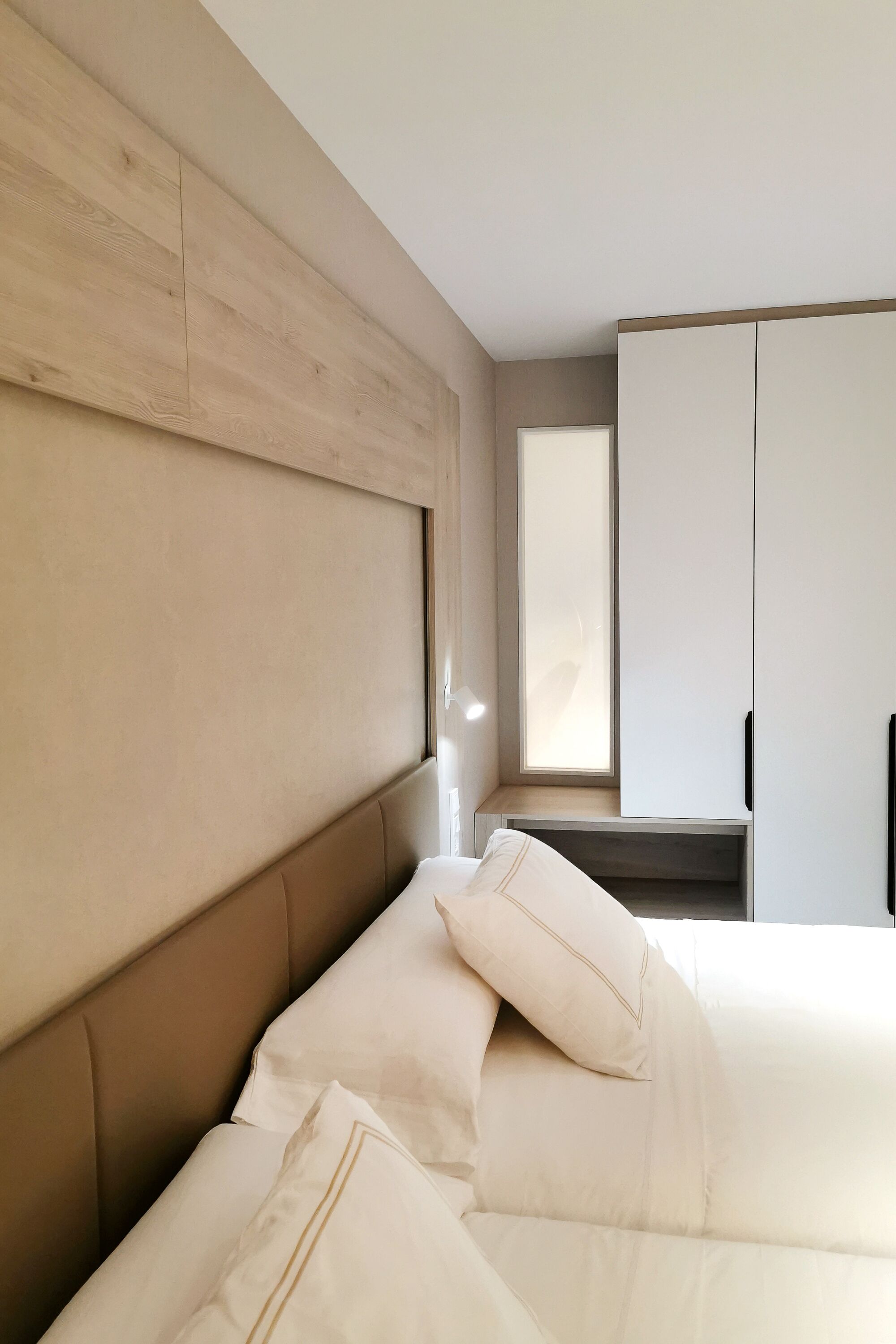 Ein modernes Schlafzimmer mit einem hölzernen Kopfteil, einem großen Fenster und einem Kleiderschrank.