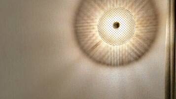 Una habitación con un escritorio de madera, un enchufe y una lámpara circular que proyecta una sombra.