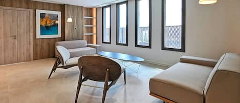Una sala de estar moderna con un sofá, un sillón, una mesita y ventanas amplias.