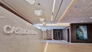 A modern hotel lobby with a marble wall, a large chandelier, and a large abstract painting. - Hotel & Spa Castillo de Peñíscola (Peniscola)