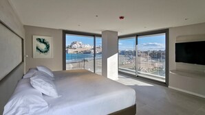 A modern bedroom with a large bed, a TV, and a view of a coastal city. - Hotel & Spa Castillo de Peñíscola (Peniscola)