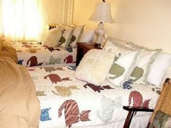 Een slaapkamer met twee bedden, elk met een bedsprei met patroon. Er is een nachtkastje met een lamp en een stoel.