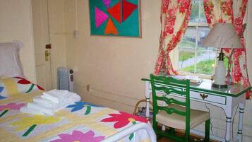 A bedroom with a bed, a desk with a chair, a window with curtains, and a painting on the wall.