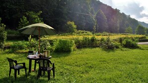A table with an umbrella, chairs, and outdoor dining setup in a grassy area with a mountain backdrop.