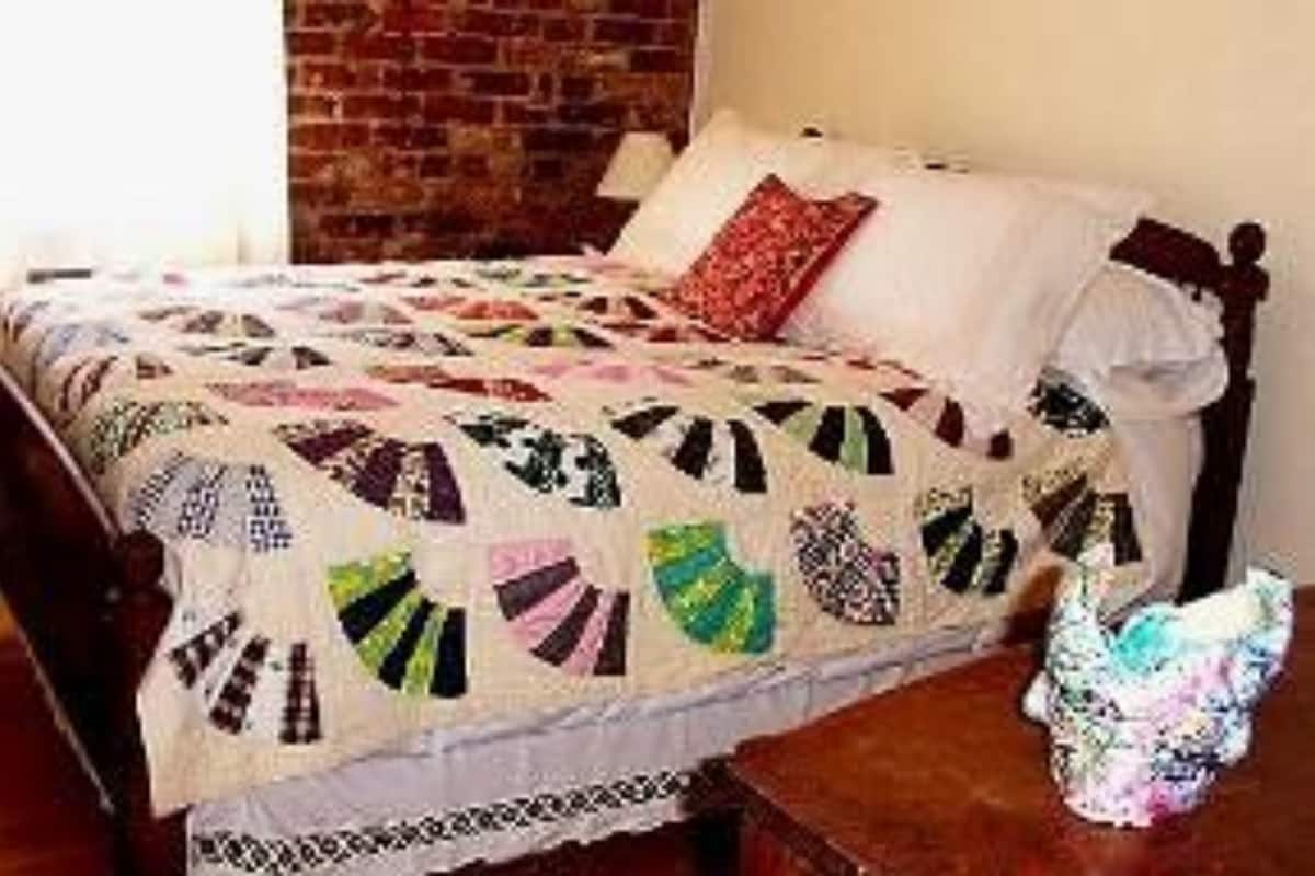 A bed with a quilt, a brick wall, and a wooden floor.