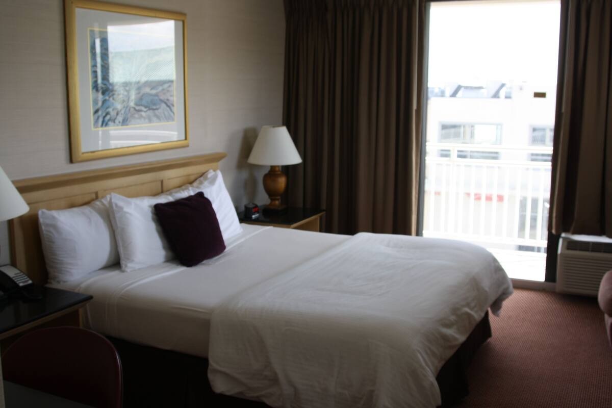A hotel room with a large bed, bedside lamps, a nightstand, a chair, and a window with curtains.