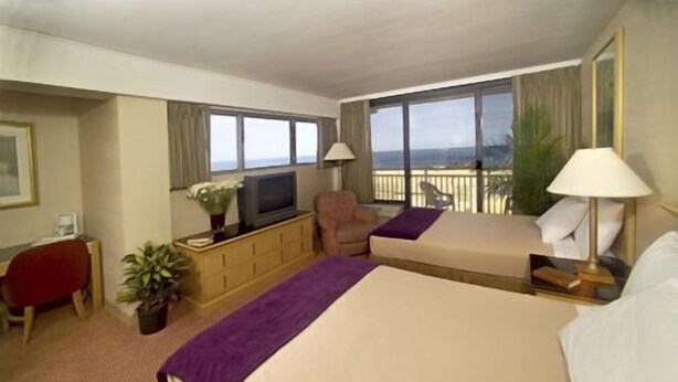 A hotel room with two beds, a TV, a desk, and a balcony with a view.
