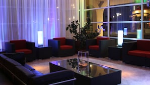 A modern lobby with black sofas and red cushions, a glass coffee table, and a large potted plant.