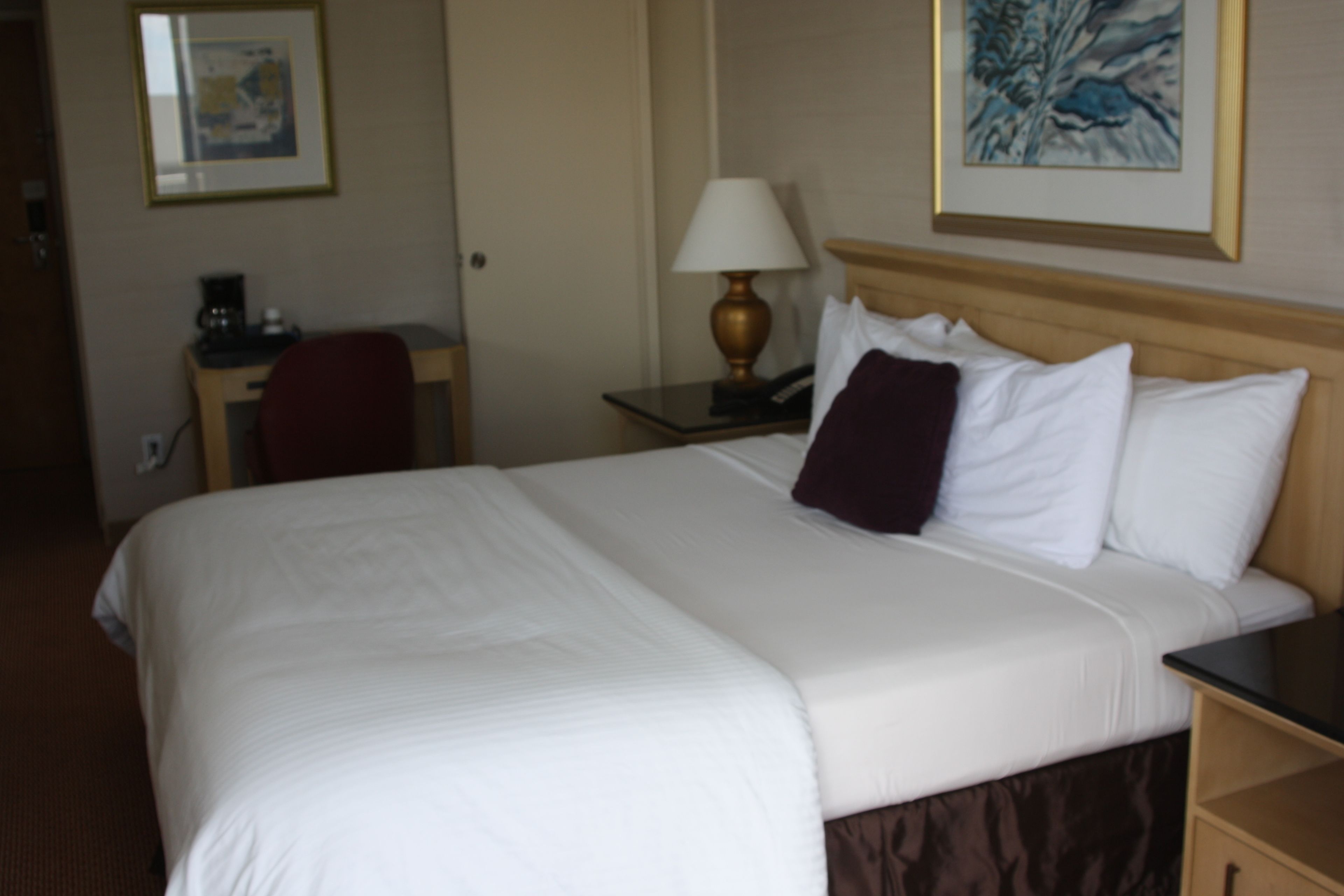 A hotel room with a large bed, a desk with a lamp, a chair, and a painting on the wall.