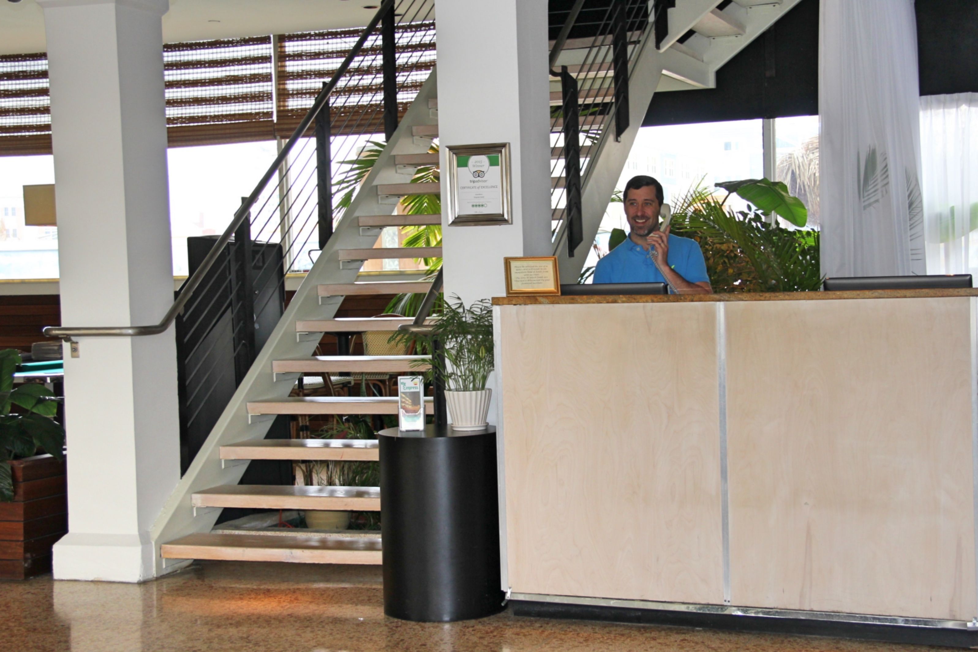 A reception desk with a staircase, potted plants, and a framed certificate on the wall.