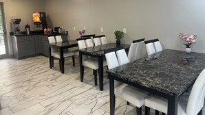 A modern dining area with a marble table and white chairs, a coffee machine, and a small plant on the table.
