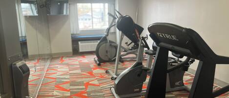 A gym with exercise equipment, a patterned carpet, and a window with a view of buildings.