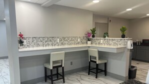A modern kitchen with a white tiled backsplash, two bar stools, a marble countertop, and a microwave.