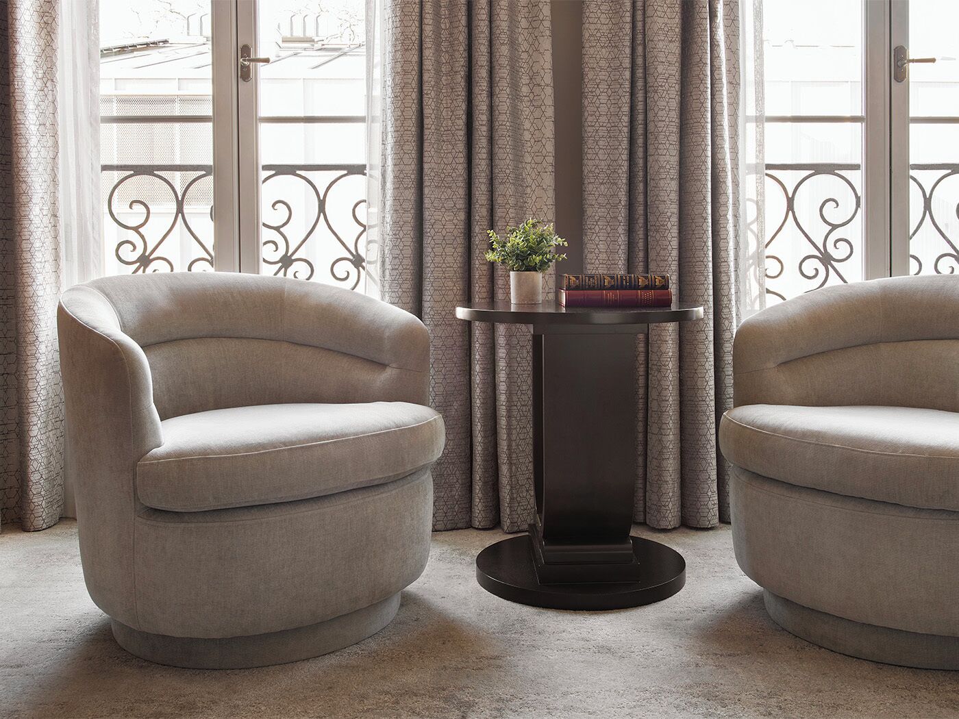 Two armchairs, a small table with a plant and books, and a view through a window with curtains.