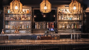Un bar con tres lámparas de mimbre colgantes, estantes llenos de botellas de licor y una encimera de mármol.