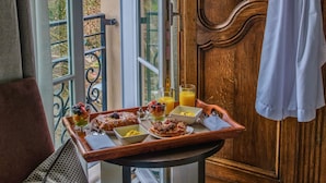 Una habitación con puerta de madera, una bata blanca colgada, una mesa de desayuno y vistas a través de un ventanal.