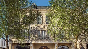 Un edificio de dos pisos con una entrada central, ventanas grandes y un balcón.