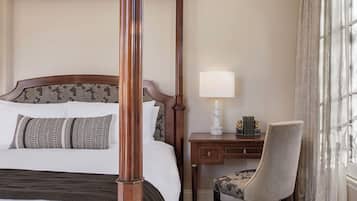 A four-poster bed with a headboard, a bedside table with a lamp, a chair, and a window with curtains.