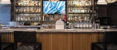 A bar area with wooden paneling, a large TV screen, and multiple liquor bottles.