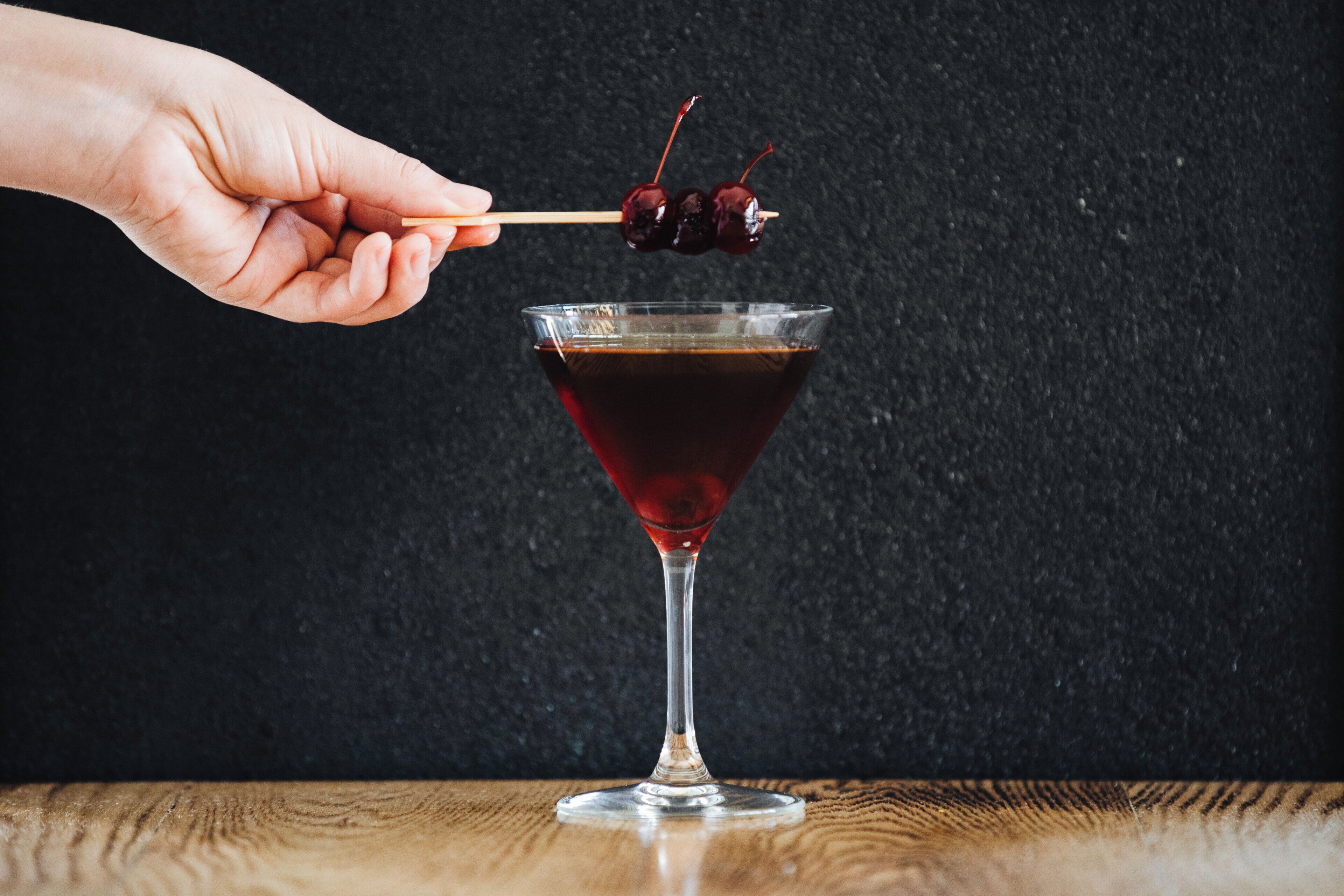 A hand holding a skewer with cherries over a martini glass.