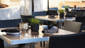 Un área de comedor al aire libre con mesas, sillas y plantas en macetas.
