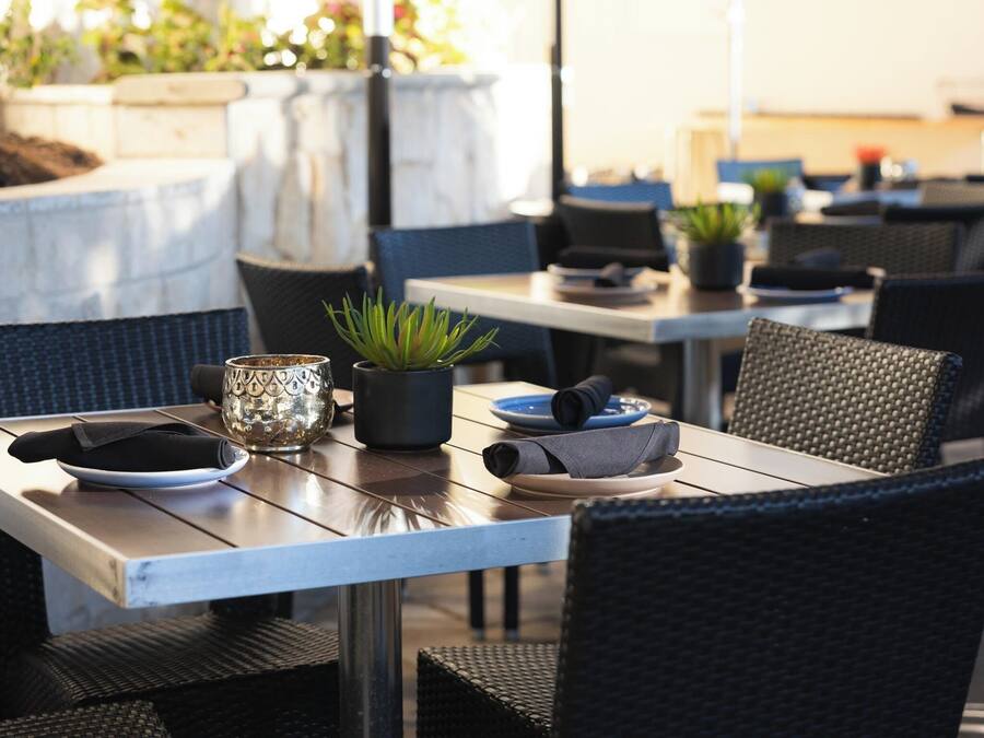 Un área de comedor al aire libre con mesas, sillas y plantas en macetas.