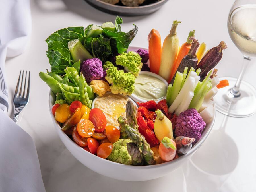 A bowl of assorted vegetables and a glass of white wine on a table.